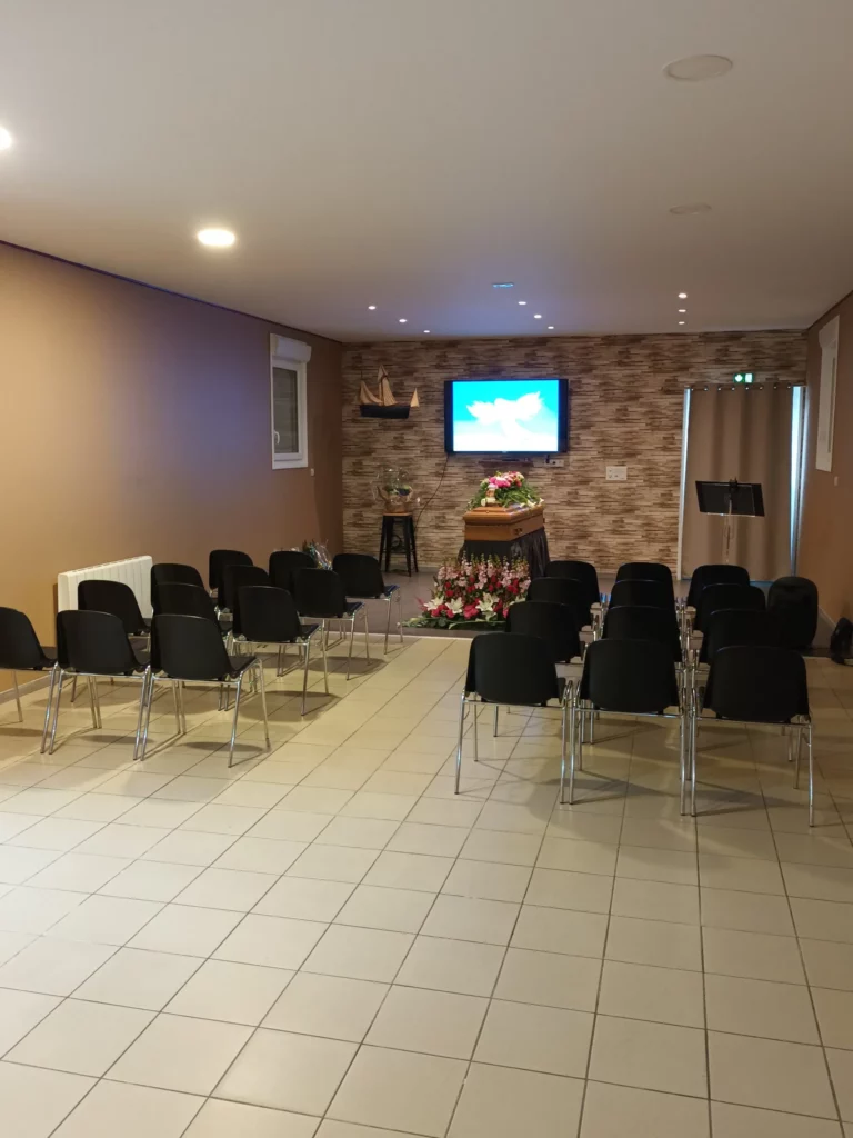 Salle d'hommage funéraire aménagée avec des rangées de chaises.