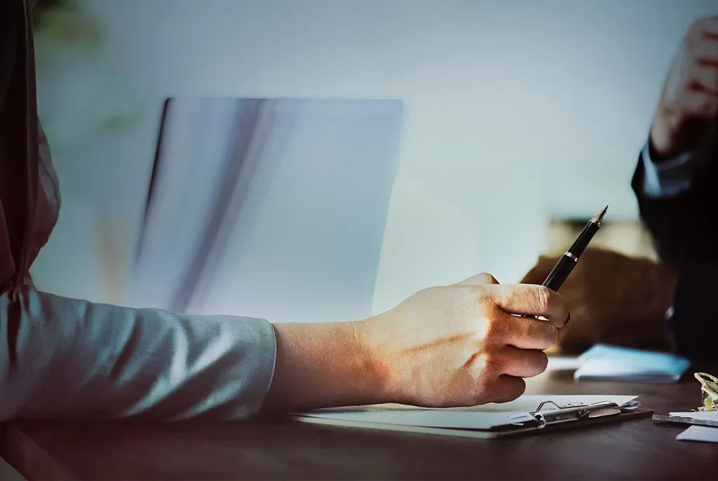 Personne rédigeant un document officiel avec un stylo lors d'un entretien.