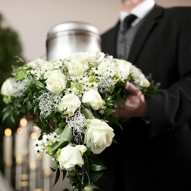 Agent funéraire tenant un grand bouquet de fleurs blanches et une urne.