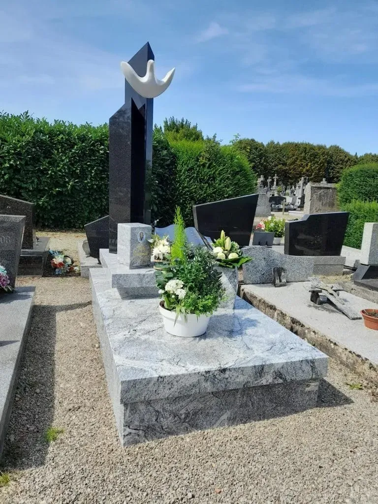 Monument funéraire moderne en granite gris clair surmonté d'une colombe.
