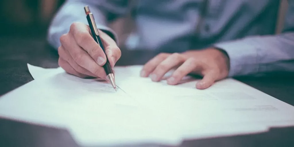 Main d'un homme signant un document officiel sur son bureau.